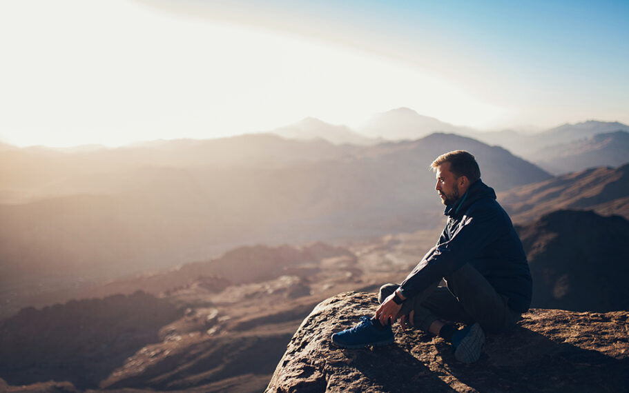 Man sits on edge of cliff on Mount Sinai and looks at sunrise in Egypt.